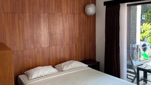 A modern bedroom with a wooden headboard, a large bed with white bedding, a small bedside table, and a view of an outdoor area with chairs and a table.