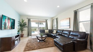 A spacious living room with a leather sectional sofa, a coffee table, and a flat-screen TV mounted on the wall. - Modern|Spacious|10br|Sleeps 20|10mintoDisney|PrivatePool|Villa (Kissimmee)