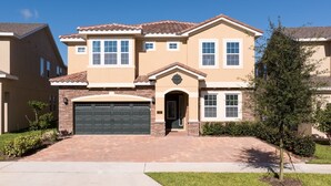 A two-story house with a brick garage, a front entrance with a small porch, and a clear blue sky. - Modern|Spacious|10br|Sleeps 20|10mintoDisney|PrivatePool|Villa (Kissimmee)