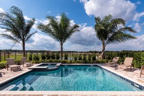 A swimming pool with lounge chairs and a hot tub, surrounded by palm trees and a view of a sports field. - Modern|Spacious|10br|Sleeps 20|10mintoDisney|PrivatePool|Villa (Kissimmee)