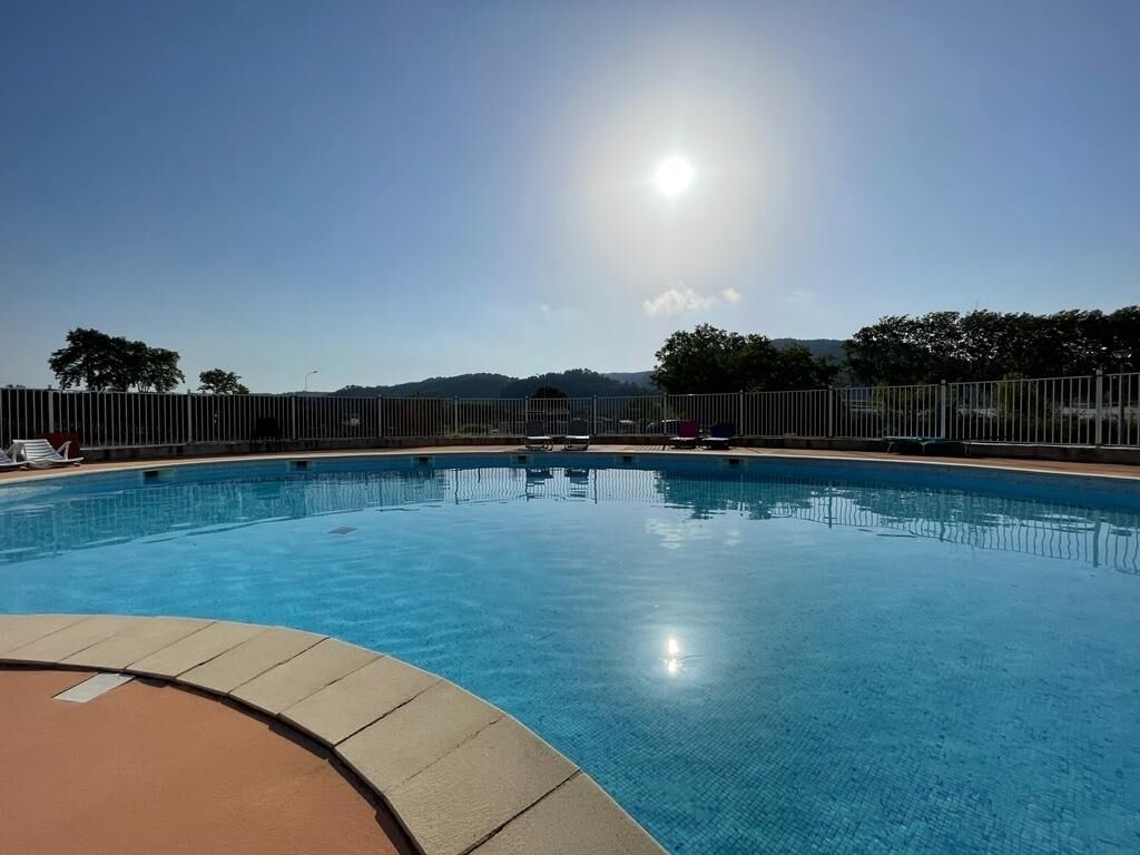 A clear blue swimming pool with a fenced area, surrounded by trees and hills in the background.