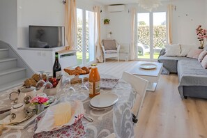 A dining area with a table set for breakfast, a sofa, and a TV in the background. - La Petite Poule Rousse - Maison avec piscine (Anduze)