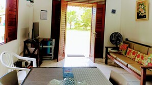 A room with a sofa, a chair, a table, a TV, and a fan. There is a door leading outside. - Recanto Feliz (Tamandaré)