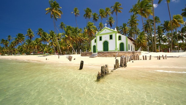 A beachside building with a green and white facade, surrounded by palm trees and clear turquoise water. - Recanto Feliz (Tamandaré)