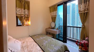 Un dormitorio con una cama, una tocador con espejo, una ventana con cortinas y un balcón con vistas a edificios altos.