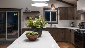 Une cuisine moderne avec un plan de travail en marbre, des meubles en bois et un grand pot de fleurs.