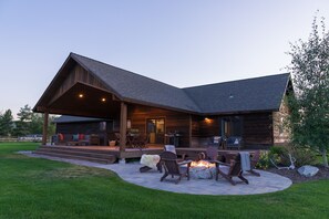 Une cabane en rondins moderne dotée d’un patio couvert, d’un espace salon extérieur et d’un foyer.