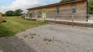 A wooden cabin with a green door, a gravel driveway, and a grassy area with chairs and a table. - Lulu Logs (Bristol)
