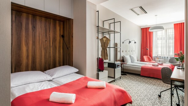 A hotel room with a wooden headboard, two beds with red bedding, a desk, a chair, and a large window with red curtains. - No.23 Premium Aparthotel (Kraków)