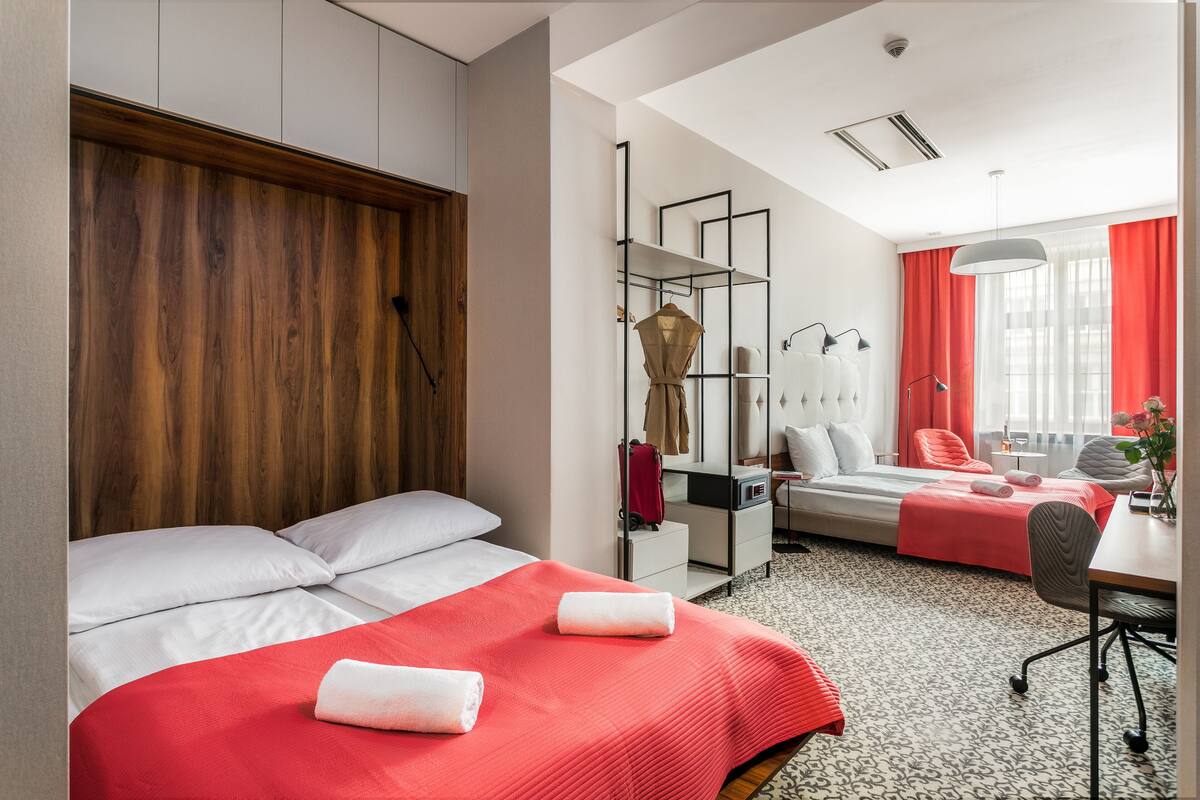Habitación de hotel con dos camas, un escritorio, una silla, un armario y una ventana con cortinas.