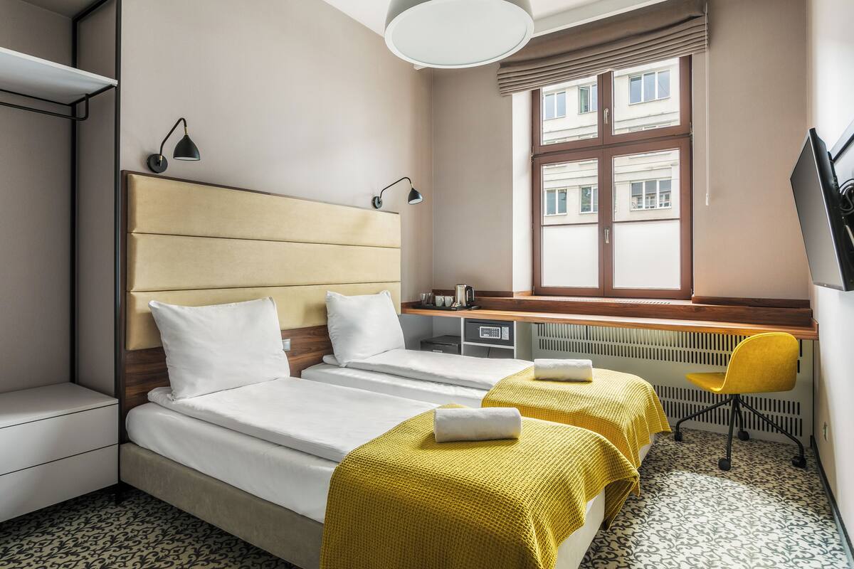Habitación de hotel con dos camas, un escritorio, una silla y una ventana con vista a edificios.