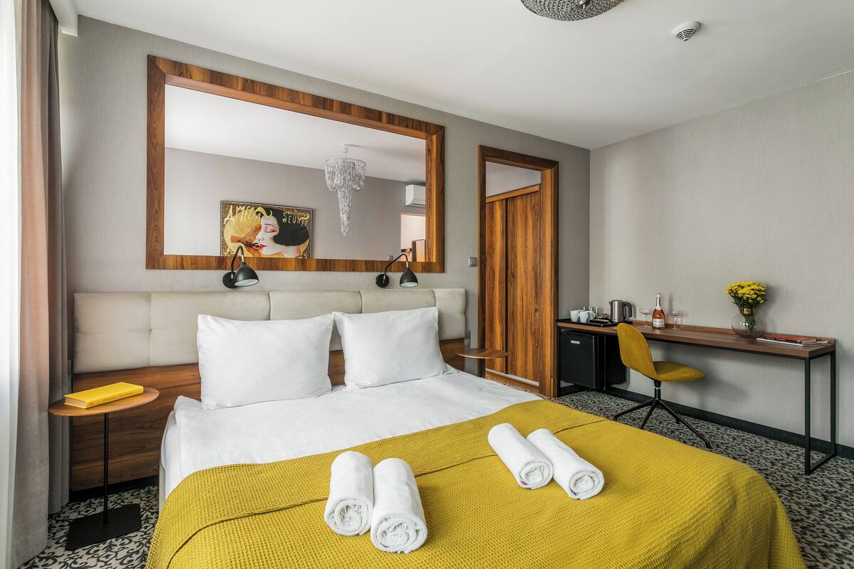 Una habitación de hotel con cama, escritorio, silla, mesita de noche, espejo y candelabro.