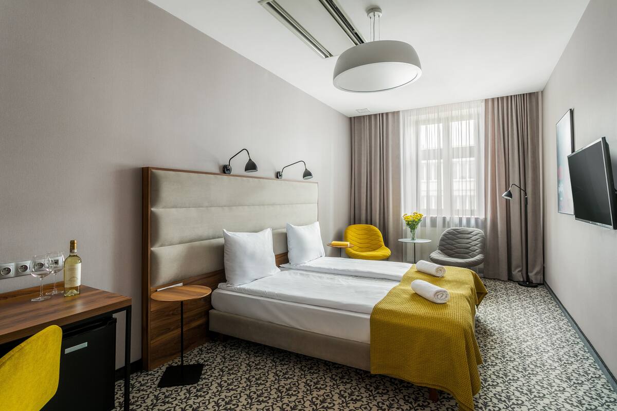 Habitación de hotel con una cama grande, un escritorio con silla, una mesita de noche con lámpara y un televisor en la pared.