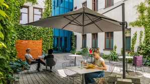 An outdoor patio with metal chairs and tables, surrounded by greenery and a building with blue and white walls. - No.23 Premium Aparthotel (Kraków)