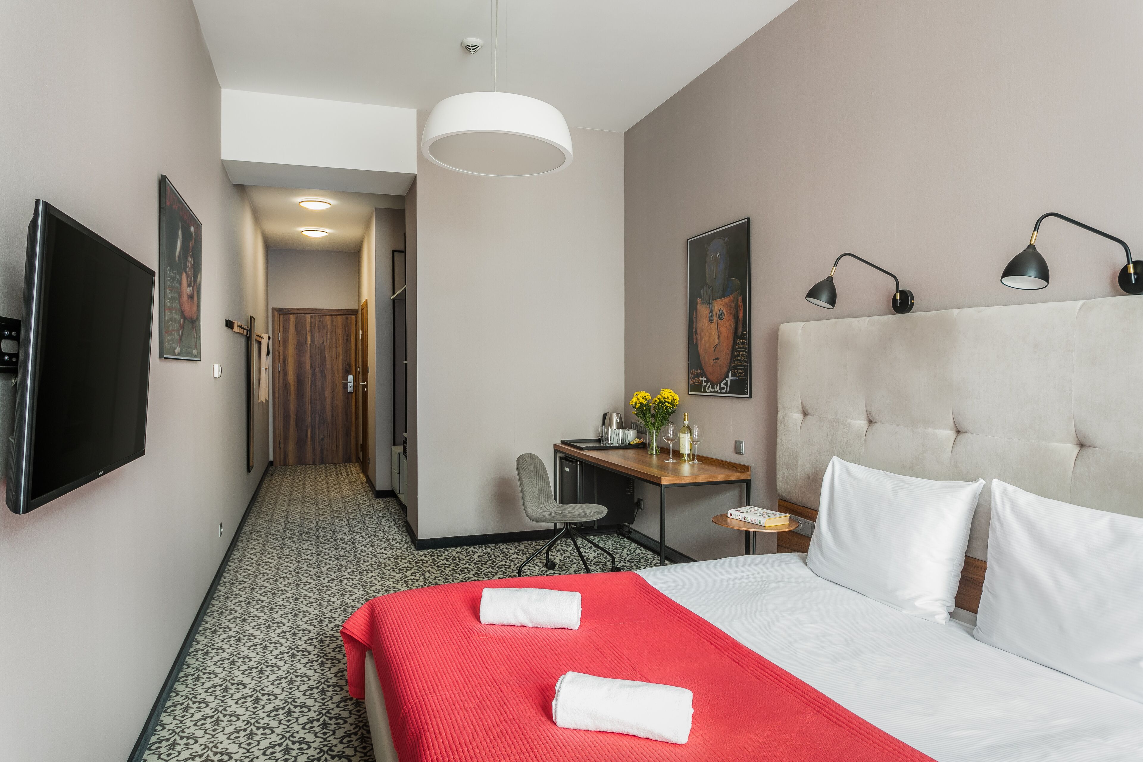 A hotel room with a large bed, a desk with a chair, a television, and a painting on the wall.