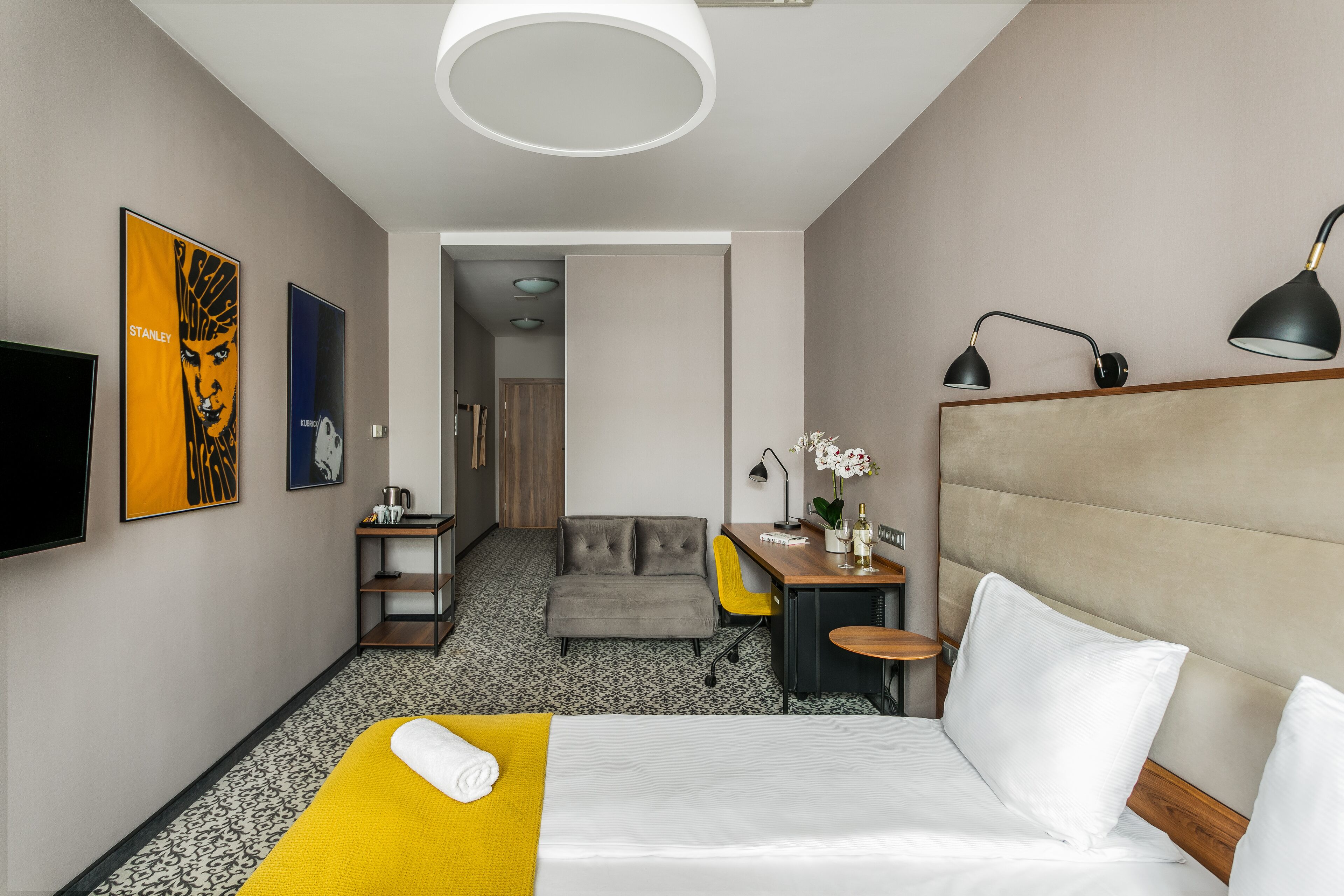 A hotel room with a bed, a desk, a chair, a TV, and artwork on the walls.