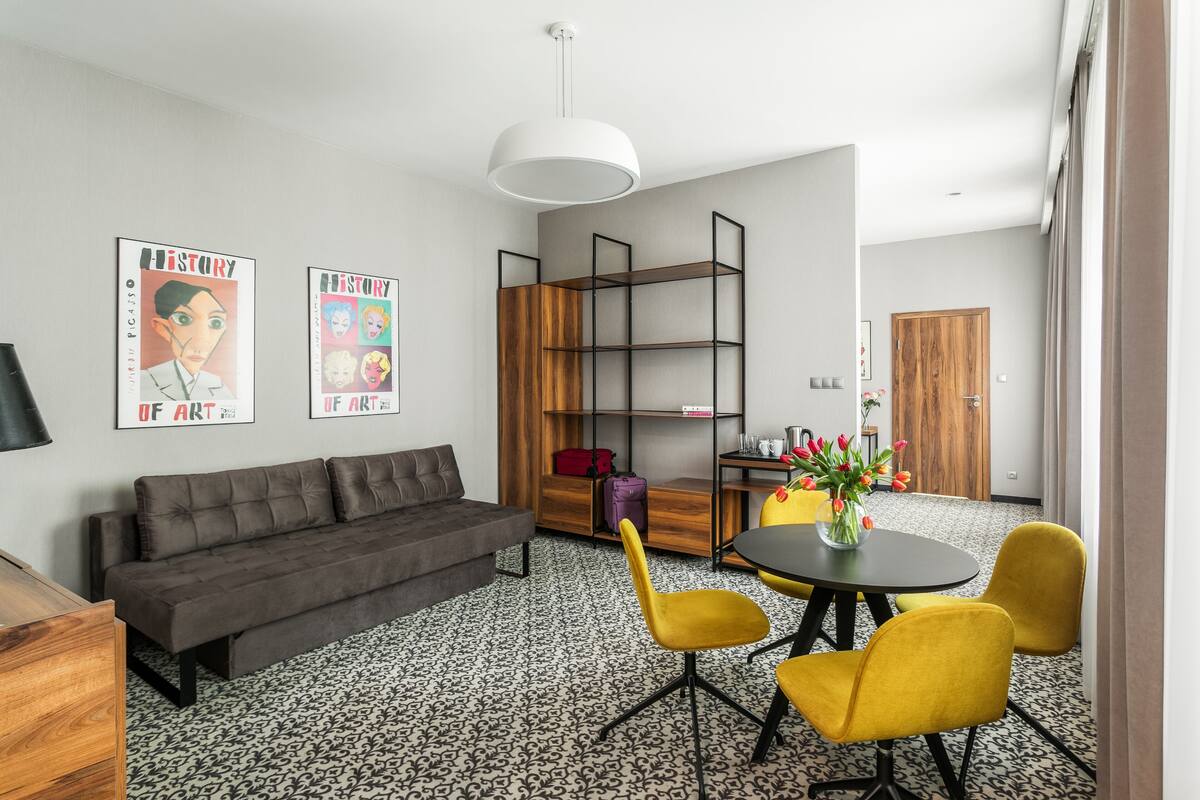 Una sala de estar moderna con un sofá, sillas amarillas, una mesa redonda y una estantería.