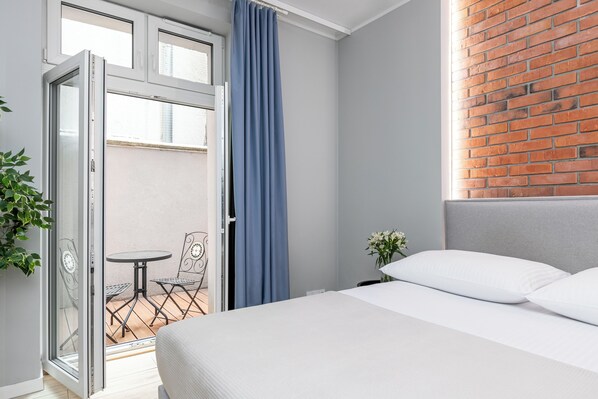 A hotel room with a bed, a balcony with a table and chairs, and a brick wall.