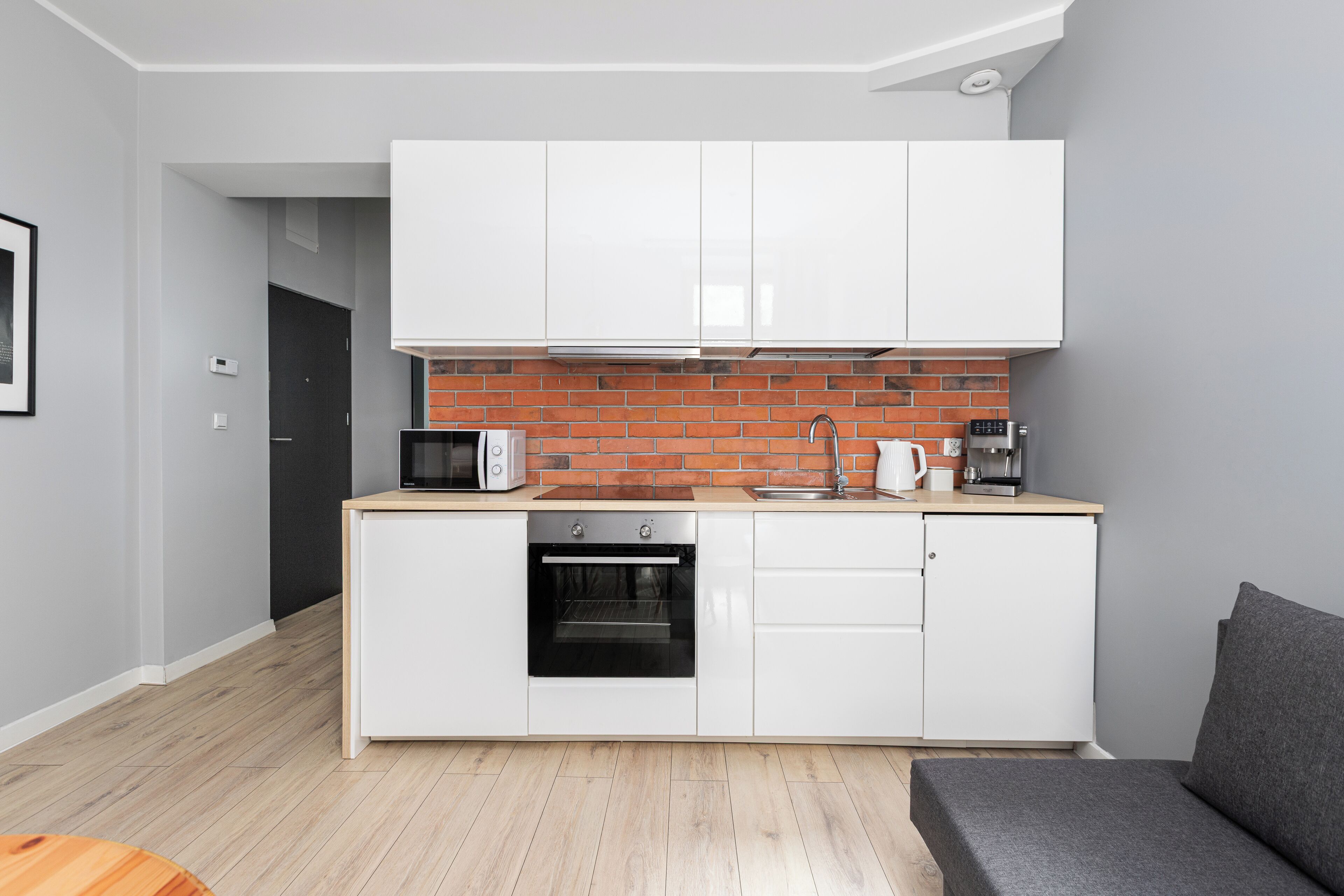 A modern kitchen with white cabinets, a brick backsplash, and a built-in oven.