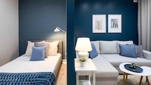 Moderni hotellihuone, jossa on sänky, sohva, pieni pöytä ja kaksi kehystettyä kuvaa seinällä.