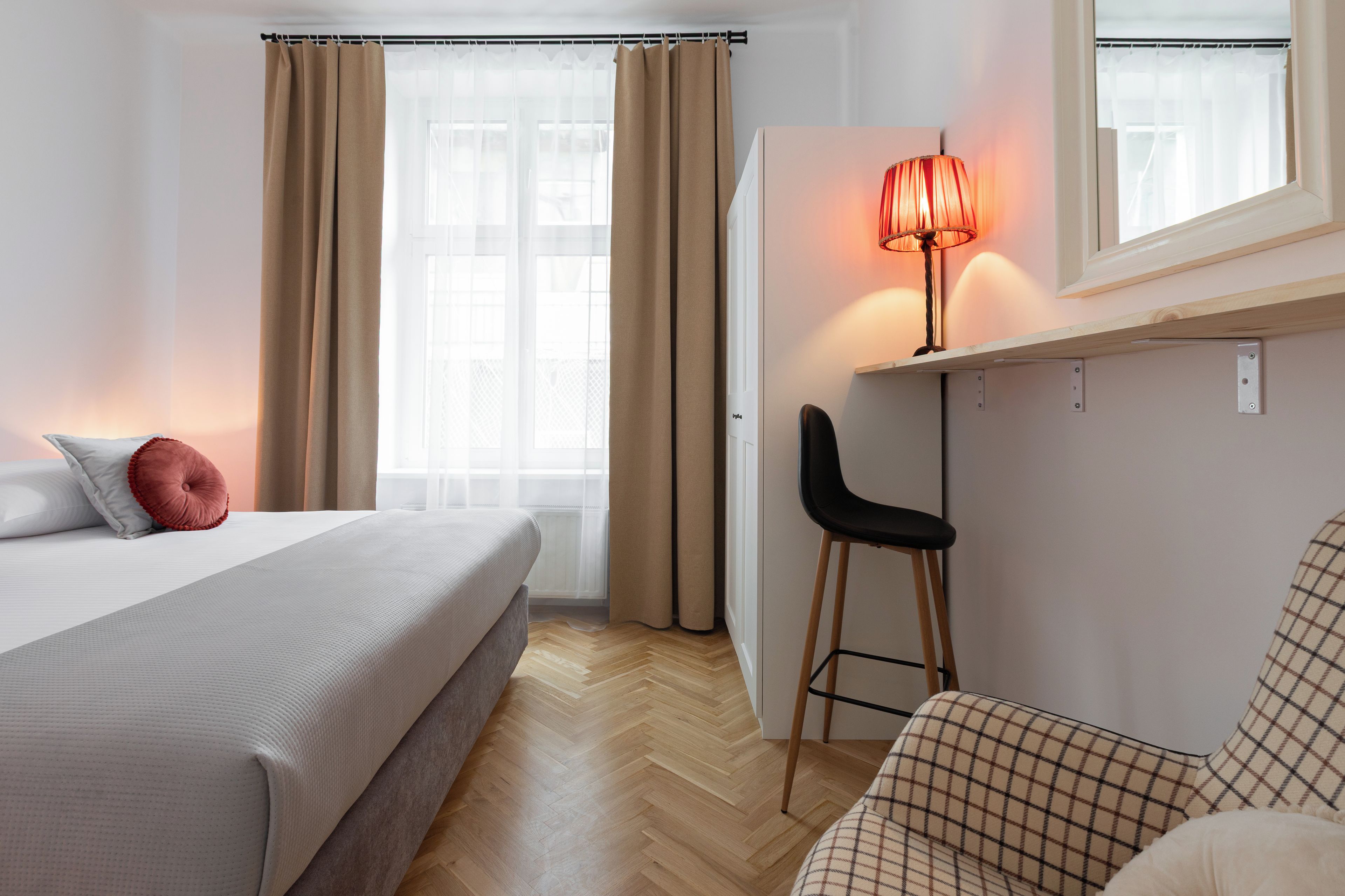Un dormitorio con cama, escritorio, silla, cortinas en una ventana y una lámpara.