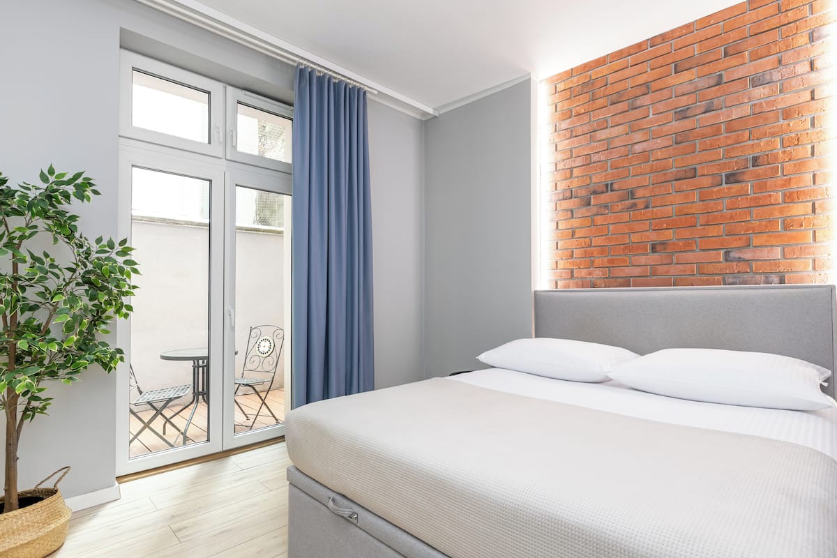 A bedroom with a bed, a potted plant, a sliding glass door, and a brick wall.