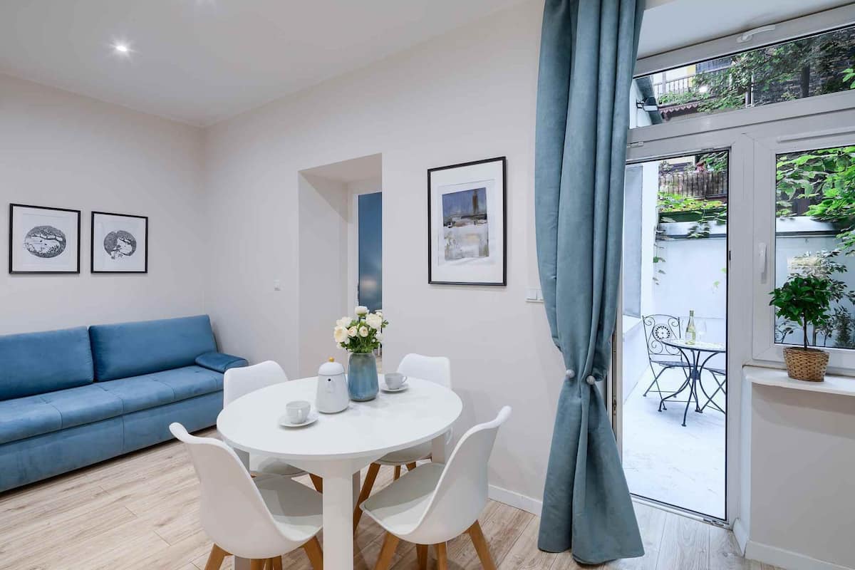 A modern living room with a blue sofa, a round white table with chairs, and framed pictures on the wall.