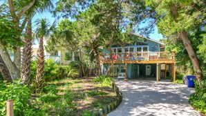 A two-story house with a balcony, surrounded by lush greenery and trees. - Turtle Hideaway- Walk to Beach & Pier! (St. Augustine)