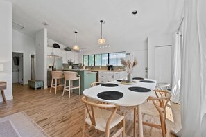 Una cocina moderna con armarios blancos, un comedor con mesa y sillas blancas, e iluminación colgante.