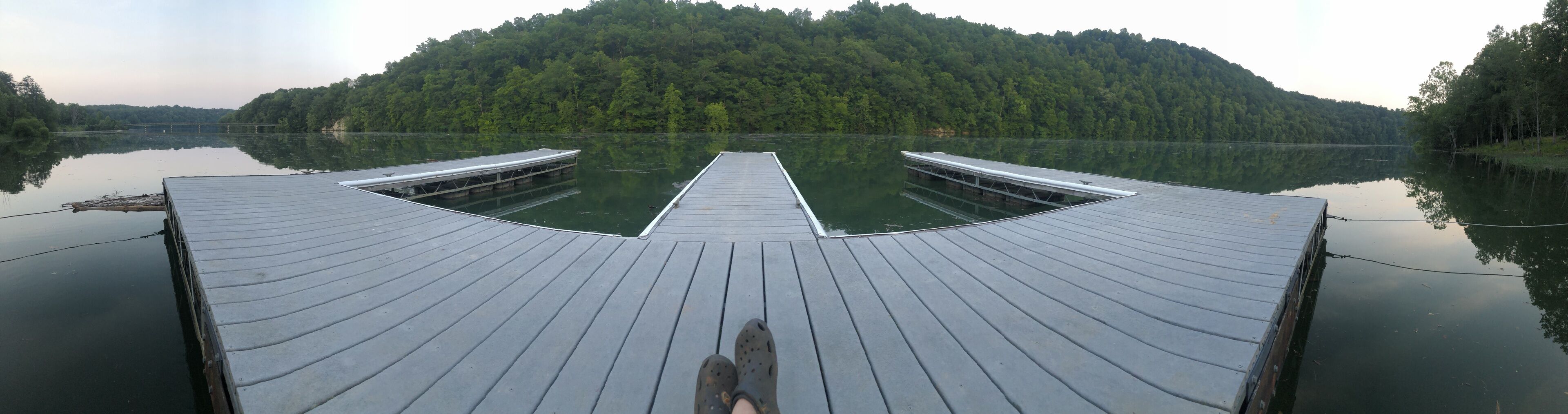 A wooden pier extending into a calm lake, surrounded by dense forest.