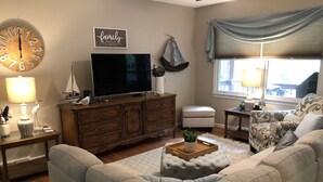 A living room with a large flat-screen TV, a wooden cabinet, a sofa, a coffee table, and a wall clock.