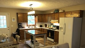 A kitchen with wooden cabinets, a white refrigerator, a stove, and a dining area with a table and chairs.