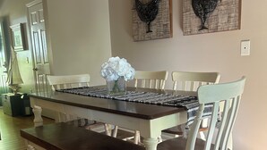 A dining area with a wooden table, white chairs, and decorative rooster wall art.