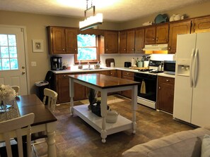 A kitchen with wooden cabinets, a central island, a refrigerator, and a dining area with chairs and a table.