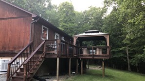 A wooden cabin with a deck and stairs, surrounded by trees.