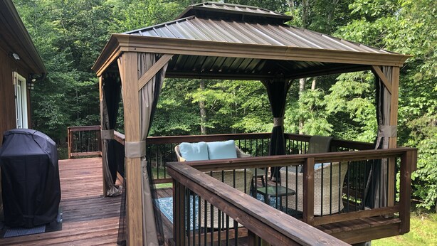 A wooden deck with a gazebo, outdoor furniture, and a grill.