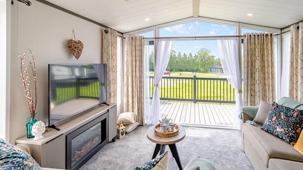 A modern living room with a TV, seating, and a view of a green landscape.