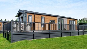 A modern mobile home with a wooden exterior, large windows, and a black metal fence.