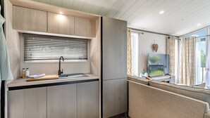 A modern kitchen with a built-in sink, window with blinds, and a flat-screen TV on a stand.