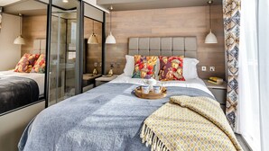 A modern hotel room with a large bed, a bedside table, a nightstand, and a window with patterned curtains.