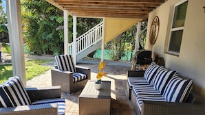 A covered patio area with wicker furniture, a grill, and a staircase leading to an upper level.
