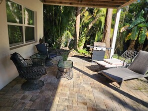 Un patio con mobiliario de mimbre, una parrilla y vistas de vegetación tropical.