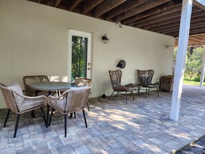 A covered patio area with wicker furniture, a table, and a door leading to a garden.