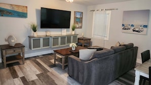 A living room with a large flat-screen TV, a sofa, a coffee table, and a dining table.