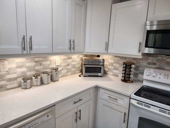 A modern kitchen with white cabinets, a stainless steel oven, a microwave, and a hexagonal tile backsplash. - Pine ridge model flat lower unit (Naples)