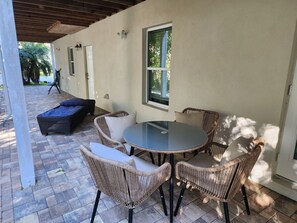 An outdoor patio with wicker furniture, a glass table, and a cushioned bench.
