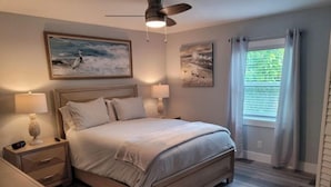 A bedroom with a bed, nightstands, a ceiling fan, and artwork on the walls.