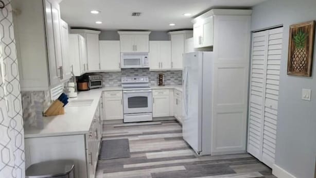 A modern kitchen with white cabinets, a microwave, an oven, and a refrigerator.