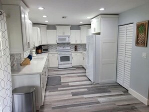 A modern kitchen with white cabinets, a microwave, an oven, and a refrigerator. - Pine ridge model flat lower unit (Naples)