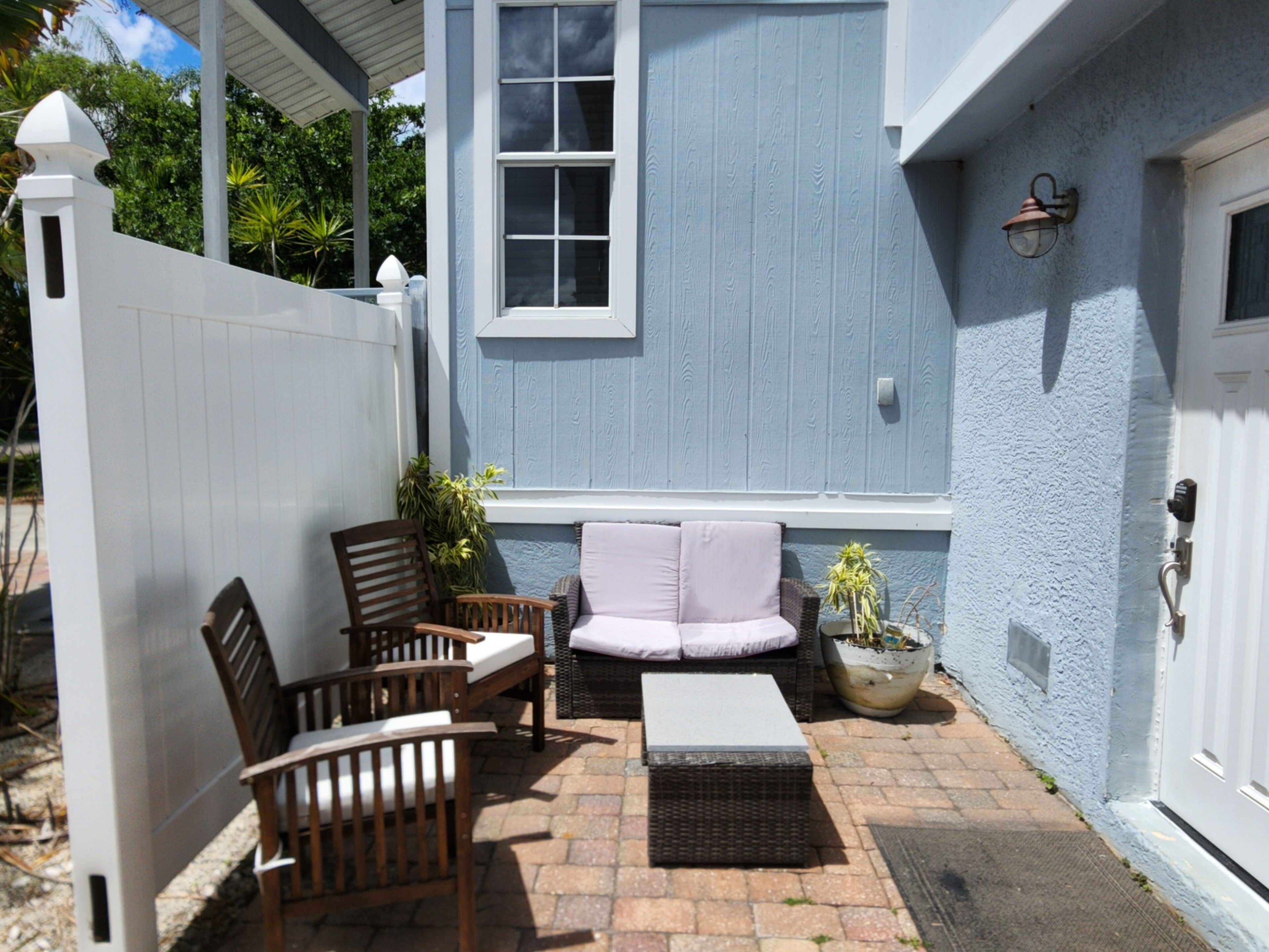 Une terrasse avec des meubles en osier, un banc rembourré et une plante en pot.